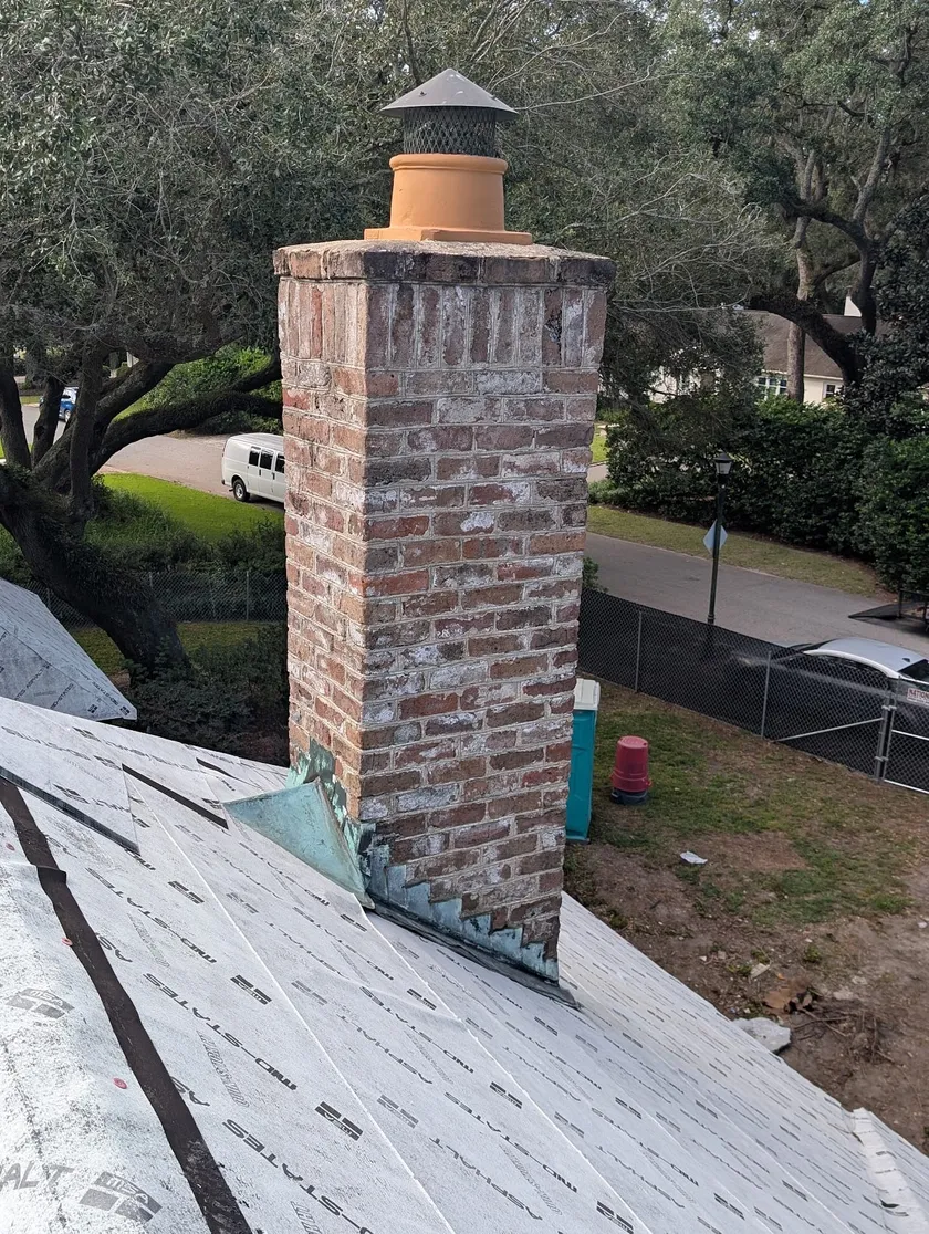 Historic brick chimney opened for rebuild above a papered roof deck, copper flashing in place