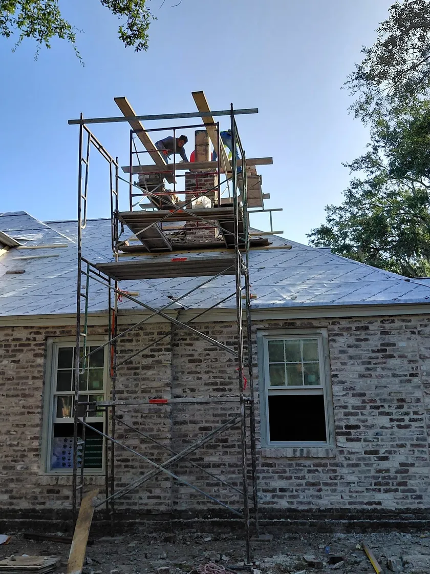 Masons on scaffolding rebuilding the chimney of a limewashed brick residence
