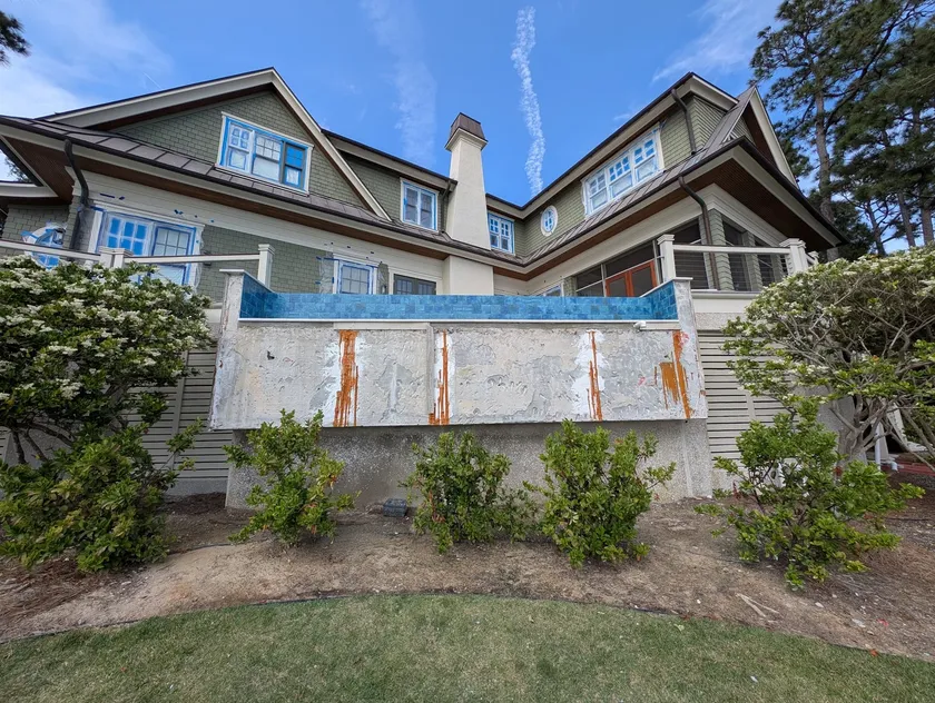 Elevated pool wall with flaking finish and rust staining below a blue tile vanishing edge
