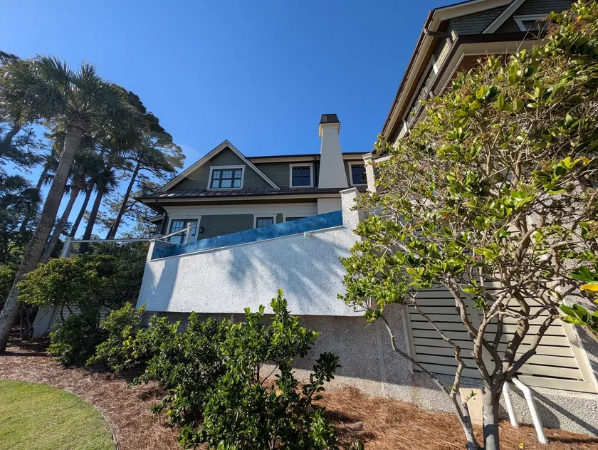 Elevated pool wall refinished beneath a blue glass tile edge on a shingle-style residence