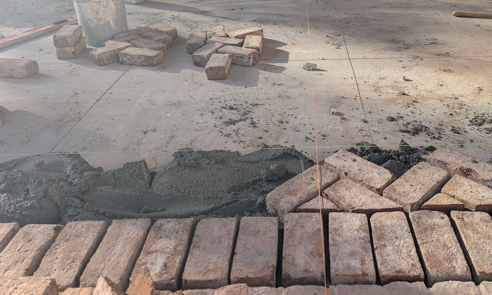 Brick being laid in a herringbone pattern on a fresh mortar bed