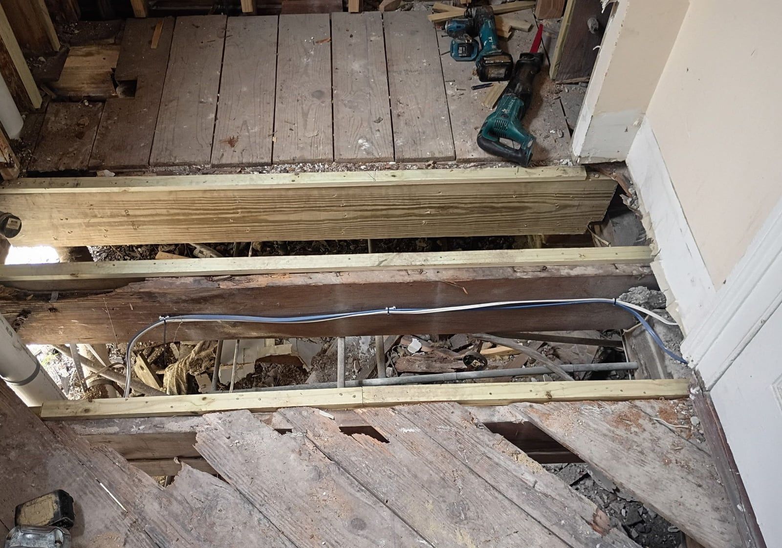 Bathroom floor opened to the framing, new joists set beside the old ones