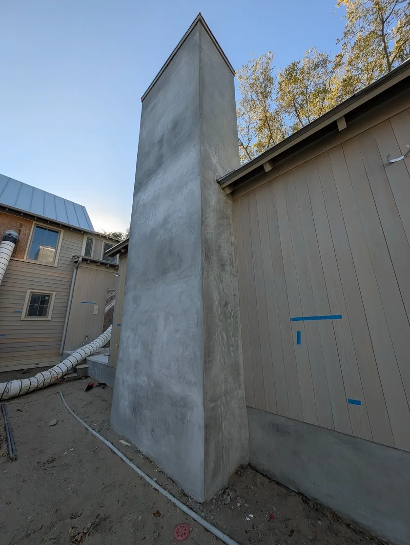 Stucco chimney mass rising beside vertical wood siding on a new build