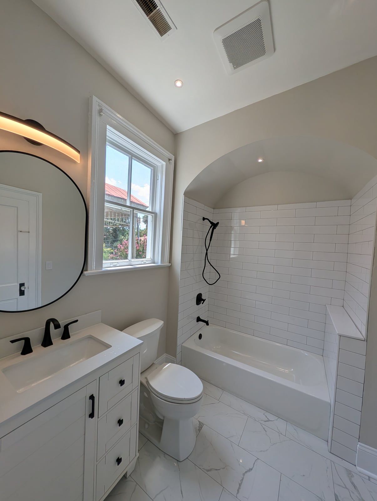Finished bath with an arched tub alcove in white subway tile, matte black fixtures and a marble-look floor