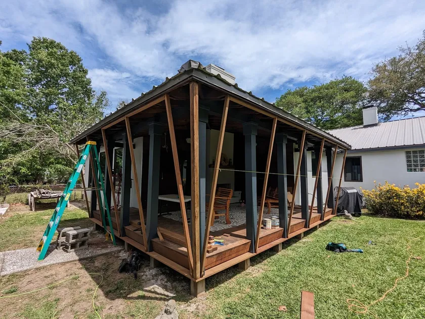 Screened room frame in progress, angled timber braces under a metal roof