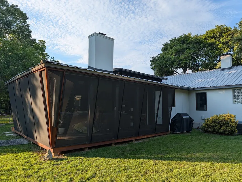 Completed screened room in daylight, dark mesh panels in an angled timber frame beside the residence