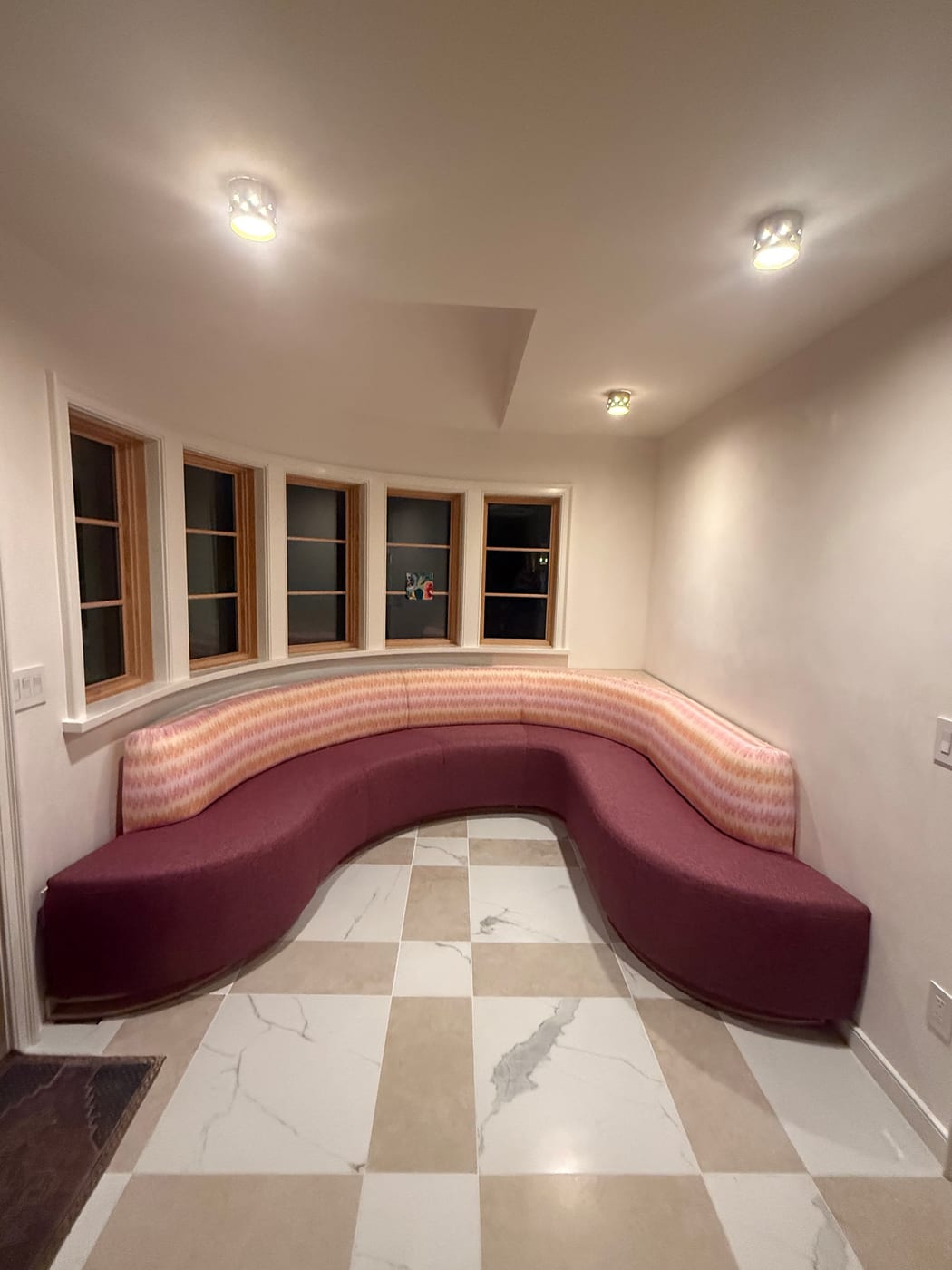 Finished upholstered banquette following a curved bay of five windows, above a checkerboard stone floor