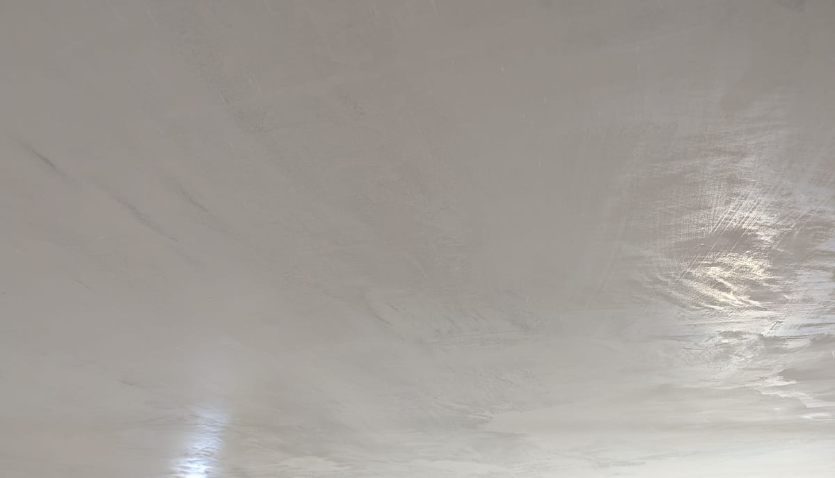 Plaster ceiling tightening under the trowel, a soft sheen rising in the light