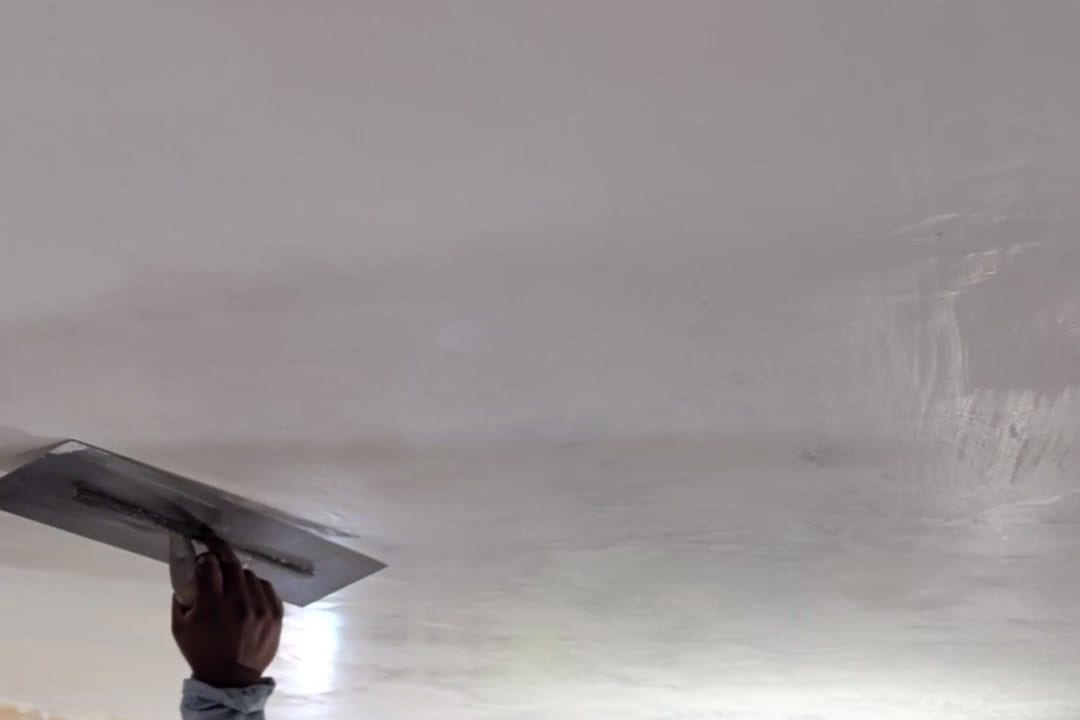 Steel trowel burnishing a plaster ceiling, pressed passes showing across the surface