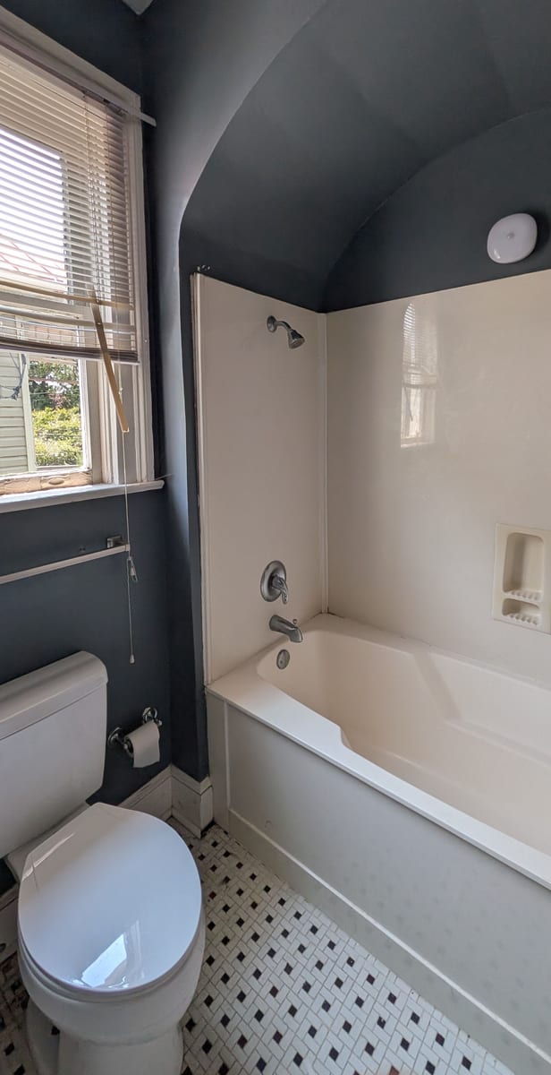 Bathroom before work, dark walls, fiberglass tub surround and small hex floor tile