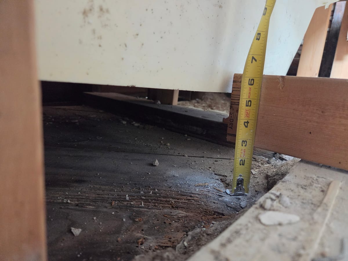 Tape measure against rotted framing beneath the removed tub