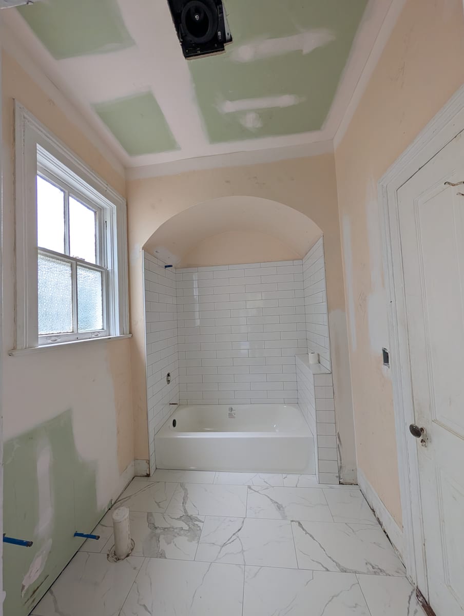 Tub alcove tiled in white subway tile with a marble-look porcelain floor, walls ready for paint