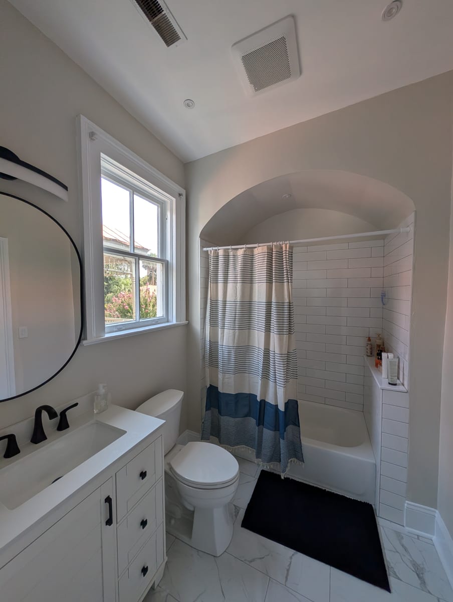 Finished bath ready to rent, vanity with matte black faucet, tub alcove with shower curtain